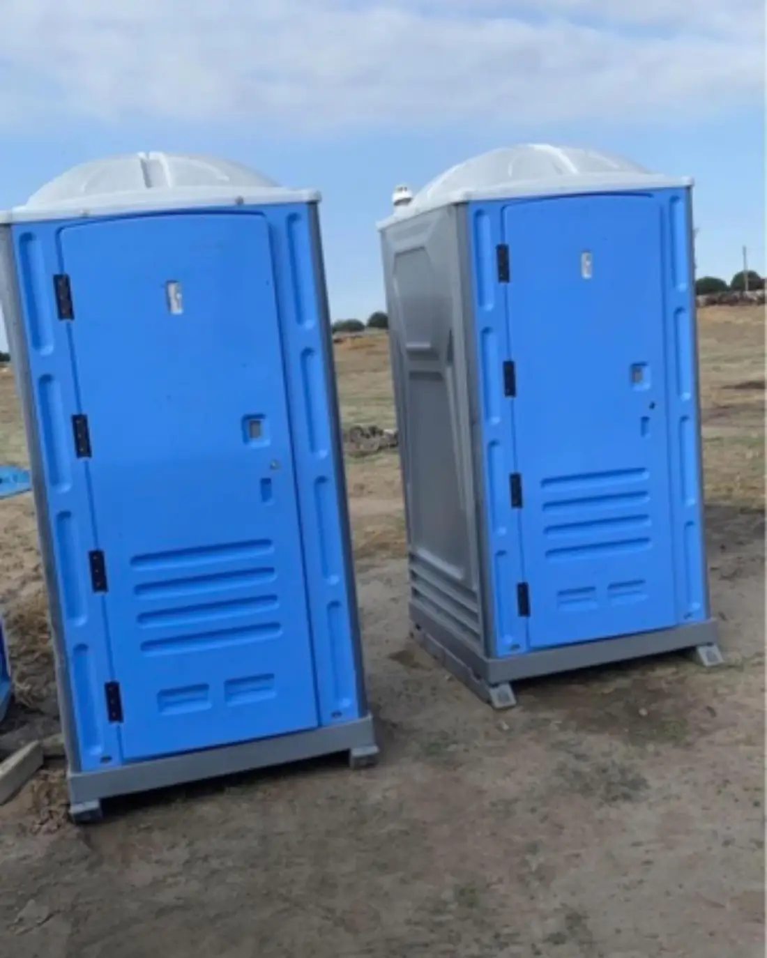 Two blue porta potties on a dirt work site
